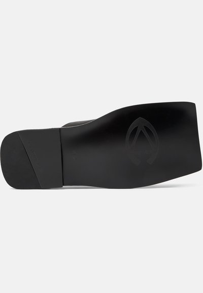 Semelle d'une chaussure de ville noire avec un talon plat, un bout carré et un logo en relief subtil près de la zone de la voûte plantaire.