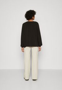Svart langermet topp med rynkede skuldre, kombinert med lysebeige vide bukser. Glatt stoff og avslappet passform, minimalistisk design.