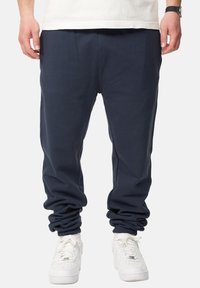 Marineblaue Sweatpants mit einem elastischen Bund und B ündchen, die einen lockeren Schnitt und weiches Fleece-Material aufweisen, kombiniert mit weißen Turnschuhen.