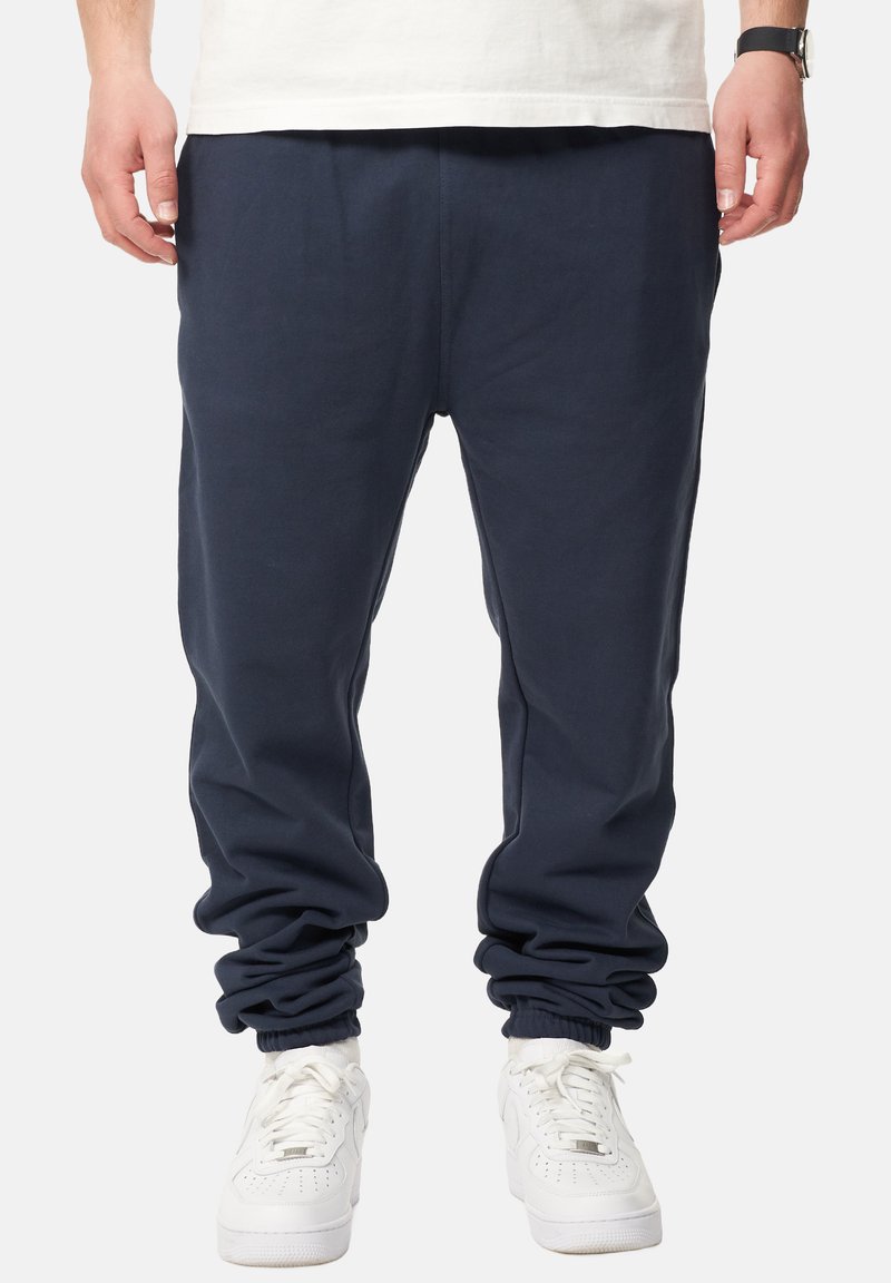 Marineblaue Sweatpants mit einem elastischen Bund und Bündchen, die einen lockeren Schnitt und weiches Fleece-Material aufweisen, kombiniert mit weißen Turnschuhen.