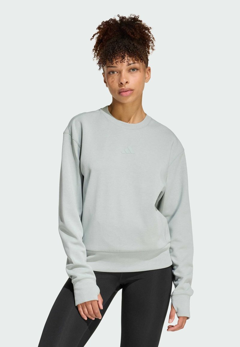 Jasnoszary sweatshirt z okrągłym dekoltem i długimi rękawami, z delikatnie wytłoczonym logo na klatce piersiowej oraz ściągaczami przy dole i na mankietach.