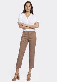Pantalons courts marron associés à une chemise blanche à col et à manches courtes. Matériau : coton lisse. Chaussures : talons en daim beige, design ouvert.