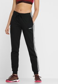 Zwarte sweatpants met witte zijstrepen, elastische tailleband en trekkoord. Materiaal lijkt zacht; heeft een logo op de linker bovenbeen.