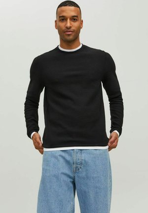 Maglietta nera a maniche lunghe con texture a coste e colletto bianco a contrasto, indossata con jeans azzurri a vestibilità ampia.