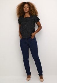 Zwarte top met pofmouwen en een gestructureerd ontwerp, vierkante halslijn; gecombineerd met donkerblauwe skinny jeans en beige puntige hakken.