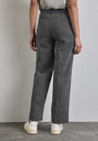 Harmaat ja mustat ruudulliset housut, joissa on korkea vyötärö, leveät lahkeet ja teksturoitu kangas; tyylitelty valkoisilla lenkkareilla.