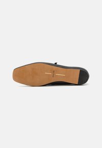 Suela de zapato negra con un borde de goma suave, plantilla color beige con marca en dorado. Patrón de relieve a lo largo de los bordes, que indica flexibilidad.