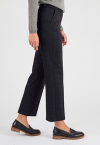 Zwart geruite broek met een getailleerde pasvorm, platte voorkant en zijzakken, gecombineerd met zwarte loafers en een grijze trui.