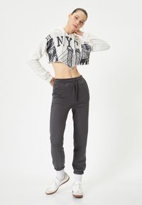 Afgeknotte witte hoodie met NYC-graphic, gecombineerd met donkergrijze joggingbroek met elastische boorden en zakken, afgewerkt met witte sneakers.