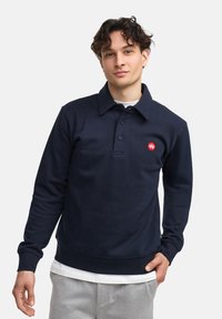 Felpa polo blu navy realizzata in misto cotone, presenta maniche lunghe, colletto e una toppa con logo rosso sul petto.