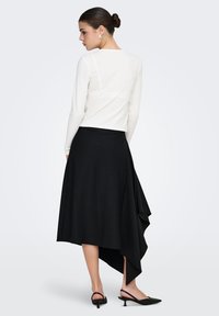 Haut blanc à manches longues et jupe asymétrique noire à rayures. La jupe présente un ourlet drapé et une légère texture ; assortie à des chaussures à talons noires.