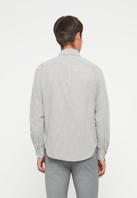 Stripet skjorte med knapper i lys grå og hvit stoff; har krage, lange ermer med knapper, og en avrundet kant.