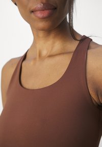 Brun atletisk tanktop med en glat tekstur, bred halsudskæring og tykke stropper, designet til komfort og bevægelsesfrihed.