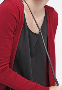 Rote Strickjacke aus weichem Stoff, mit langen Ärmeln, Knöpfen und einem lässigen Schnitt, getragen über einem schwarzen Oberteil mit rundem Ausschnitt.