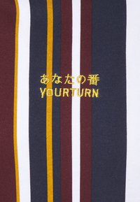 Tessuto rigato con colori marrone, blu navy, bianco e senape. Il testo ricamato in giallo recita "YOURTURN" e caratteri giapponesi.