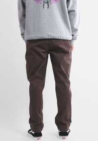 Chinos en coton marron avec une coupe droite et des détails sur la couture latérale, assortis à un sweat-shirt gris clair avec un motif graphique rose.