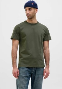 T-shirt verde oliva a maniche corte in cotone, con scollatura rotonda e vestibilità leggermente ampia, abbinato a jeans in denim blu.