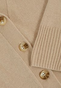 Cardigan a maglia beige con grandi bottoni crema, dettagli a costine e una texture morbida. Vista ravvicinata del tessuto e della disposizione dei bottoni.