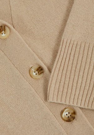 Beige stickad cardigan med stora krämfärgade knappar, ribbat detalj och mjuk struktur. Närbild av tyget och knappplaceringen.