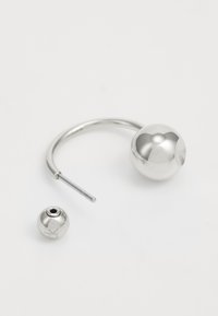 Pendiente de aro de plata con un diseño de bola pulida. Incluye una bola más pequeña y desmontable con un agujero central para la sujeción. Textura suave.