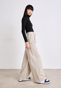 Haut ajusté noir à manches longues associé à un pantalon beige à jambes larges, avec des plis, et des baskets texturées de couleur neutre avec des touches noires.