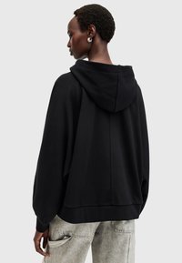 Sudadera negra con capucha, de corte holgado, con tejido texturizado y un detalle en la costura trasera. Combinada con pantalones cargo gris claro.