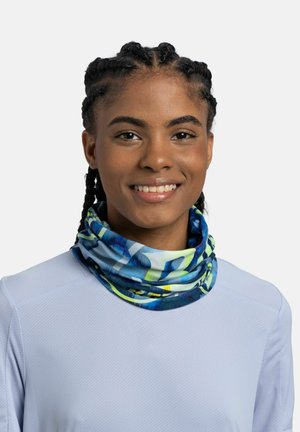 Joven mujer con el pelo trenzado sonriente, lleva una camiseta azul clara y un pañuelo para el cuello con un patrón multicolor azul y verde.
