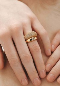 Juego de anillos de oro que presenta una banda texturizada y redondeada junto a una banda lisa con una piedra preciosa transparente en el centro, exhibido en una mano.