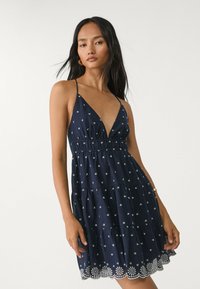 Granatowa sukienka warstwowa z cienkimi ramiączkami, głębokim dekoltem w kształcie litery V, haftem srebrnych gwiazdek oraz falbaniastym koronkowym wykończeniem.