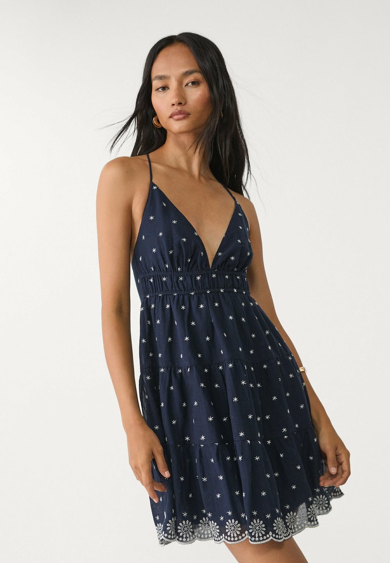 Granatowa sukienka warstwowa z cienkimi ramiączkami, głębokim dekoltem w kształcie litery V, haftem srebrnych gwiazdek oraz falbaniastym koronkowym wykończeniem.