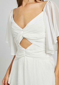 Weißes Kleid mit V-Ausschnitt, gerafftem Oberteil und schwingendem, gefälteltem Rock. Durchsichtige, flatternde Ärmel und seitliche Cut-out-Details werten das Design auf.