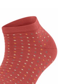 Korallefarbene Knöchel-Socke mit geripptem Bündchen, verziert mit einem Muster aus mehrfarbigen Punkten in Gelb, Grün und Beige auf einem strukturierten Stoff.