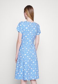 Vestido floral azul com mangas curtas e saia rodada. Apresenta padrões florais brancos. A vista traseira mostra um corpete ajustado e uma textura suave.