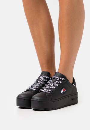 Zapatillas de plataforma negras con material sintético texturizado, que cuentan con cordones a rayas en blanco y negro y un parche con el logo en el costado.