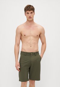 Olivenfargede shorts laget av lett stoff, med to sidelommer, knappelukking og rett ben-design. Ingen synlige mønstre.