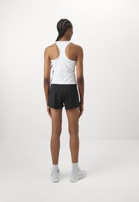 Atasan olahraga tanpa lengan berwarna putih dipadukan dengan celana pendek hitam. Atasan tersebut memiliki desain punggung pemacu, dan celana pendeknya pas dengan pinggang elastis.