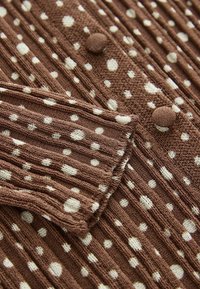 Tissu tricoté marron avec des côtes verticales et des pois blancs ; présente des boutons et un tricot texturé qui accentue le design.