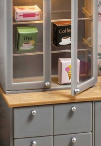 Mobiletto da cucina in plastica grigia con top in legno; le porte in vetro rivelano scatole di cibo colorate in rosa, verde e nero con grafiche stampate.
