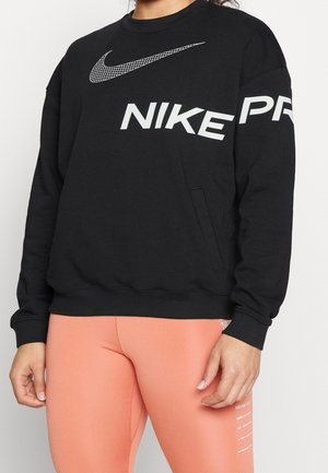 Person iført en sort Nike sweatshirt med hvidt logo og ferskenfarvede leggings med hvid tekst på låret.
