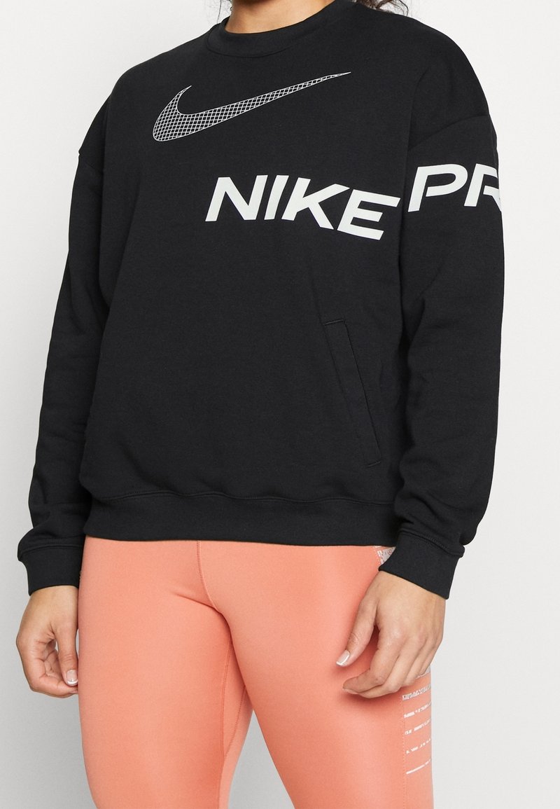 Personne portant un sweat-shirt noir Nike avec un logo blanc et des leggings couleur pêche avec un texte blanc sur la cuisse.