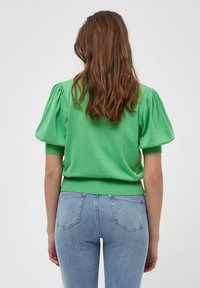 Zelený pletený svetr s krátkým rukávem a vypouklými rukávy, s žebrovaným lemem a hladkou strukturu, zkombinovaný se světle modrými skinny jeans.