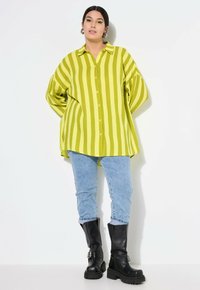 Camicia oversize a righe verdi e gialle con chiusura a bottoni, abbinata a jeans azzurri chiari e stivaletti con tacco chunky neri.