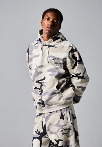 Camo hoodie en broek in grijs, beige en zwart. Voorzien van een trekkoordcapuchon en een frontzak met logo-details. Zachte, katoenmix stof.