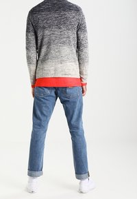 Stickad tröja med gradient från marinblå till ljusgrå, röd nederkant. Kombinerad med ljusblå denimjeans, uppvikta vid anklarna, bärs med vita sneakers.