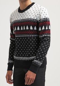 Stickad tröja med svart bas och mönster i vitt, rött och grått, inklusive snöflingor och träd, samt ribbstickad rund nacke och mudd.