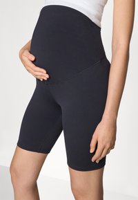 Shorts da maternità neri realizzati in tessuto elasticizzato, con una vita alta che si adatta a una pancia in crescita e una texture liscia.