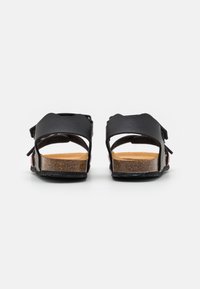 Sandalias de cuero negro con correas ajustables, plantilla de corcho y diseño de parte trasera abierta. Suela plana con detalles texturizados para mayor agarre.