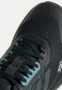 Chaussure de sport noire et bleu sarcelle avec dessus en mesh, lacets noirs et "300" imprimé sur le côté près de la semelle.
