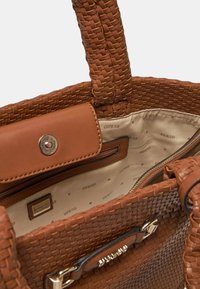 Borsa a tracolla intrecciata marrone con dettagli in pelle liscia. Presenta una tasca con zip e accessori in metallo. L'interno foderato mostra un sottile motivo con logo.