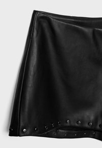 Čierna kožená minisukňa s kovovými nitmi po dolnom okraji, vystavená na svetlom pozadí.